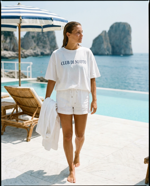 Giulia walking the marble pool deck of a private swim club above Positano, wearing the Club di Nuoto tee.