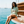A woman on the polished teak stern of a wooden gulet off the Bodrum coast at noon, wearing the Bar Negroni Oil Green Boxy Tee.