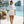 A woman walking the marble pool deck of a private swim club above Positano, the Faraglioni rocks softened in the distance, wearing the Club di Nuoto Positano boxy tee.